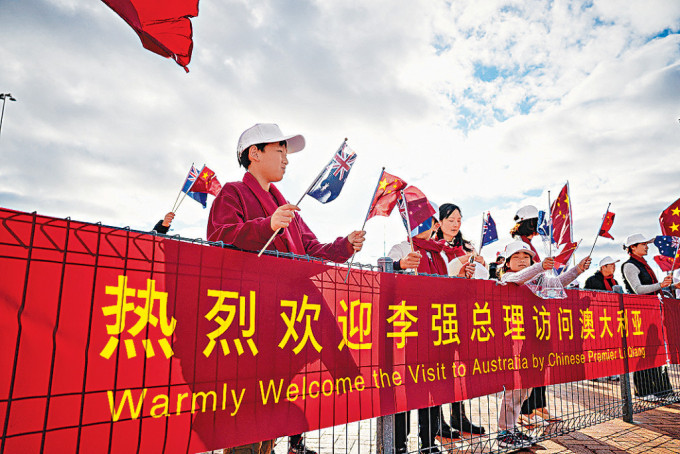 當地華人揮舞旗幟歡迎李強到訪。