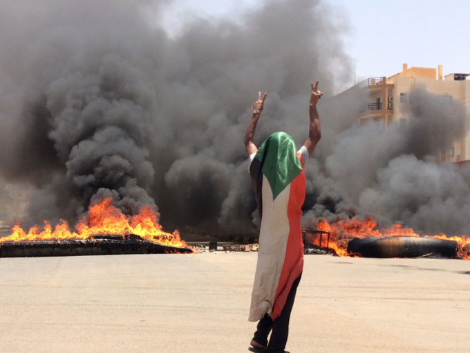 一名戴著苏丹国旗的示威者在燃烧的轮胎和碎片前摆出胜利手势。AP