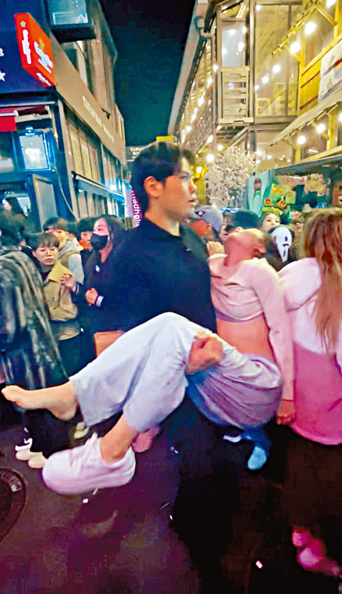 梨泰院因人踩人事件场面混乱，一名男子抱着一名疑失去知觉的女子等候救援。