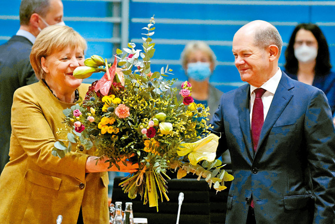 德國總理默克爾昨出席極可能是最後一場內閣會議前，從社民黨黨魁兼現任財長肖爾茨手中接過花束。