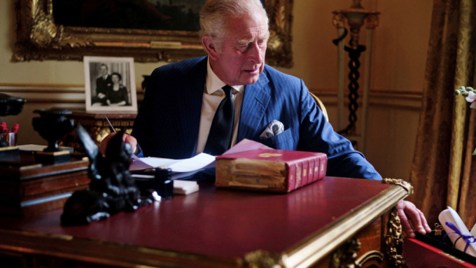 查理斯三世坐在书桌前一只手按在「红箱」边。AP