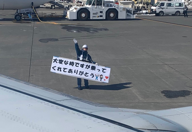 機場職員揮手向機上旅客道，橫額寫著「在這困難時刻，你們仍搭乘本航空，感謝各位支持」。 網圖