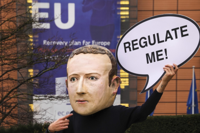 抗争者戴著Facebook CEO朱克伯格的面具，在欧盟委员会外面举著Regulate me标语。ap图