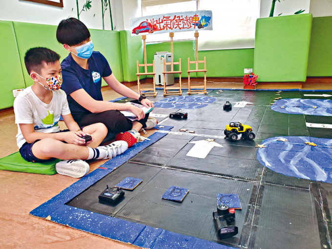鄧智杰（右）參考海洋公園遙控車遊戲概念，用紙皮建賽道，設計「逃出氣候迷陣」攤位遊戲。