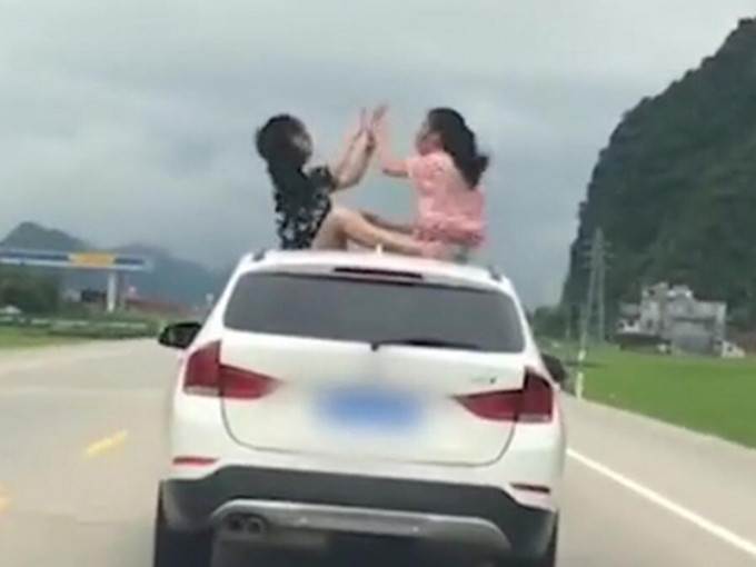 兩名女生坐在行駛中的私家車車頂上玩猜枚。　網上圖片