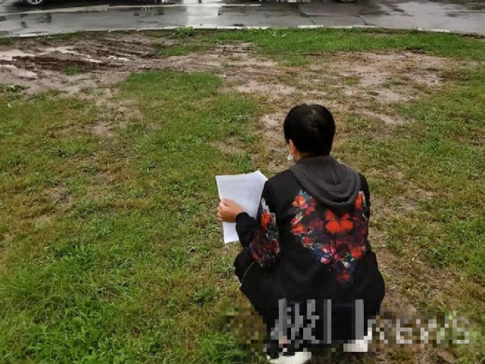 遇害学生的母亲抱着儿子照片，默默地蹲在大学校门外的草坪上，画面令人神伤。 （网上图片）