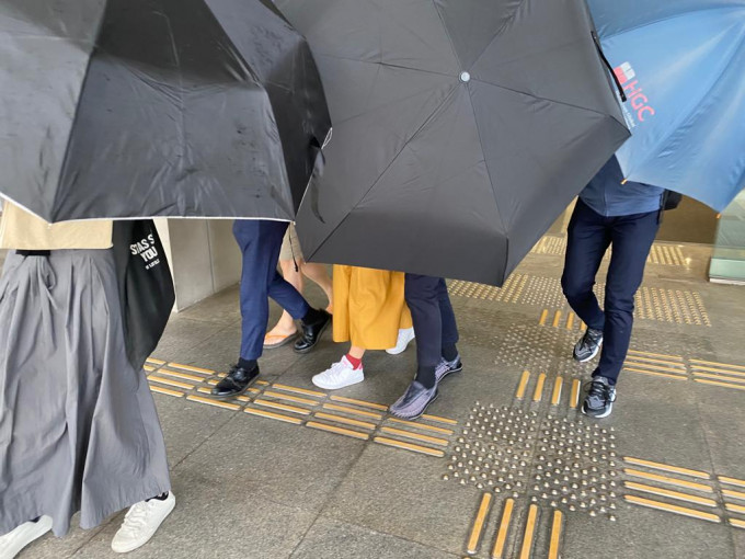 被告（左二）在伞阵掩护下离开法院。张旭珊摄