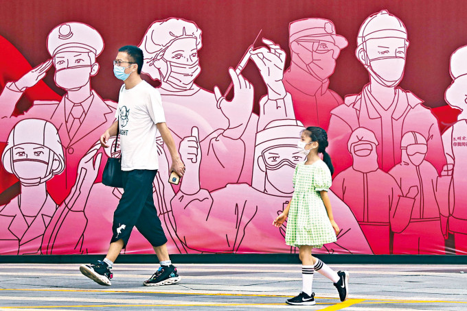 ■南京戴口罩的市民和小童在街头防疫宣传画前经过。
