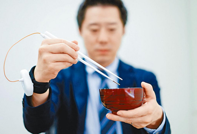 日本麒麟控股公司职员， 示范使用提升咸味的电子筷子。