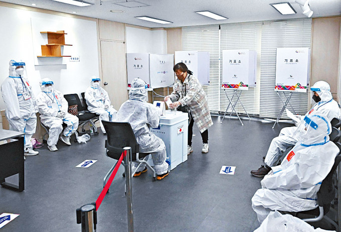 新冠確診者在首爾投票時，票站人員均穿上防疫保護衣。