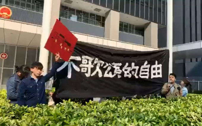 香港眾志成員早上爬上政總東翼前地的花槽掛起示威橫額。香港眾志facebook