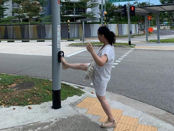 新加坡有自私大媽以腳代手「踩」紅綠燈掣，引來網民炮轟。(網圖)