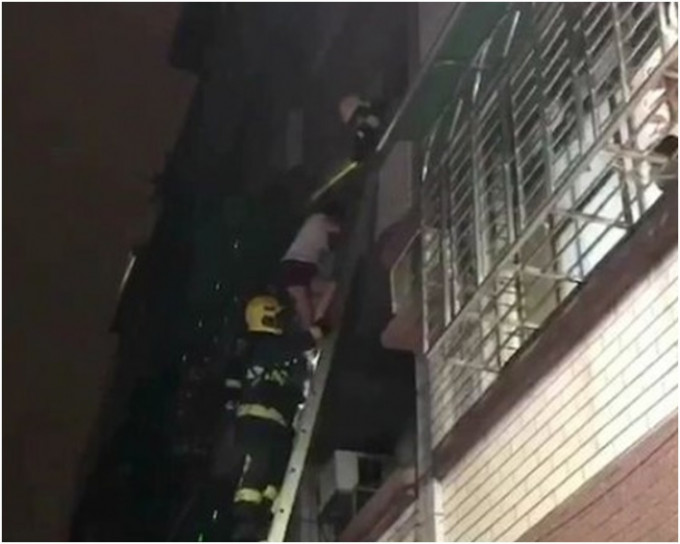 消防员架起双节铝梯协助受困居民逃离火场。