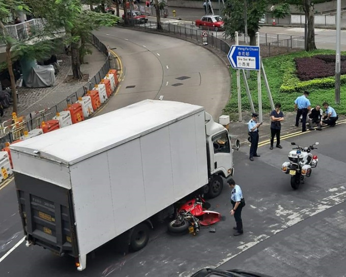 電單車翻側倒地，幾乎捲入貨車車底。