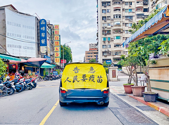 ■一輛汽車後方貼着「告急 人民要疫苗」的布條，昨天在台北街頭穿梭。