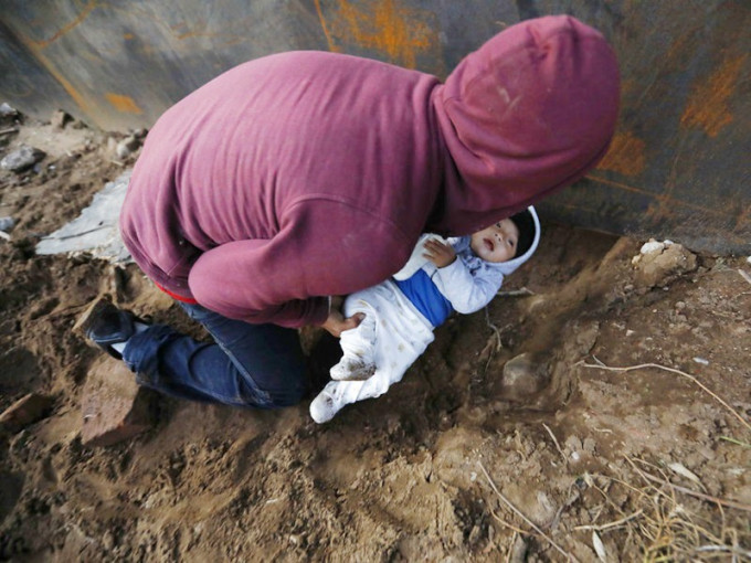 一名難民試圖將只有8個月大的兒子放進圍牆下的小坑道，交給已經進入美國的女友。AP圖片