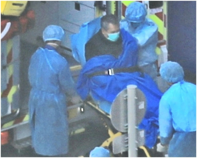 男子由穿上保护衣的救护人员送上救护车。