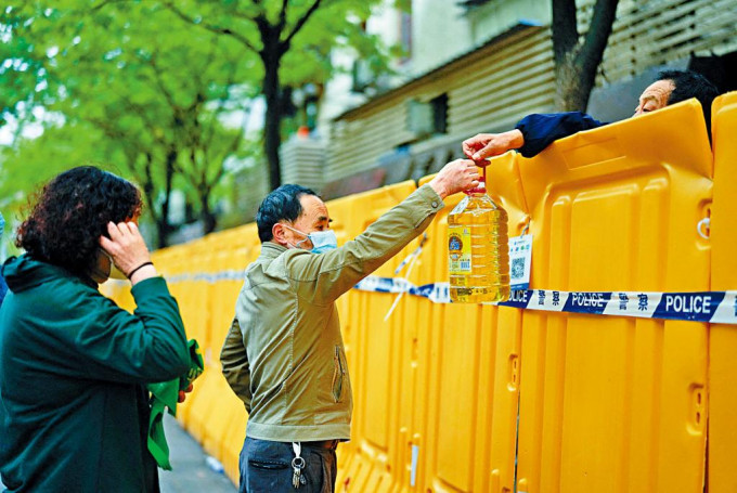上海居住在隔离区的民众，从友人手上拿取物资。