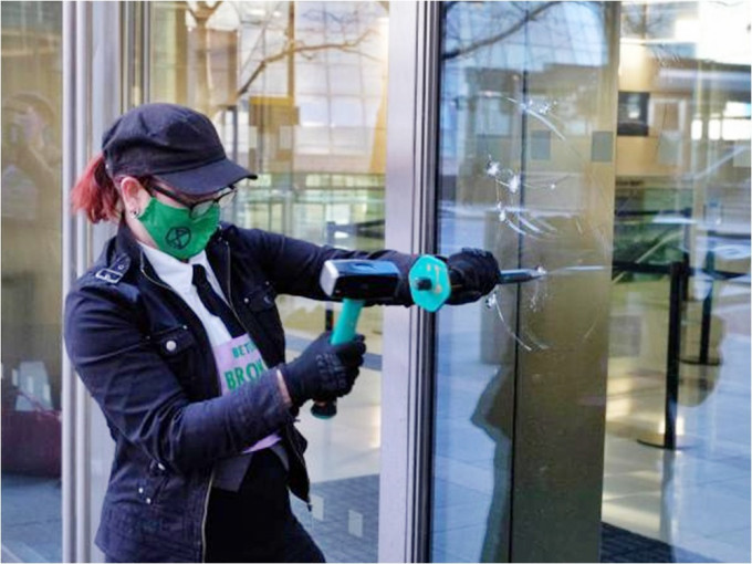 環保團體「反抗滅絕」的示威者用鎚仔打破銀行的玻璃窗。網圖