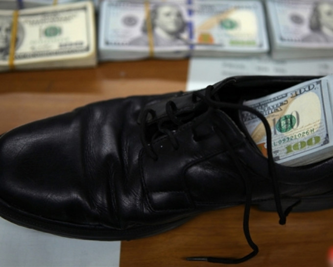 女子將一疊美元藏於一隻男鞋。網上圖片