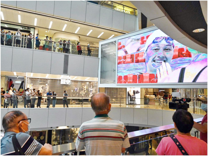 市民在大型商场的大电视旁，为何诗蓓打气。