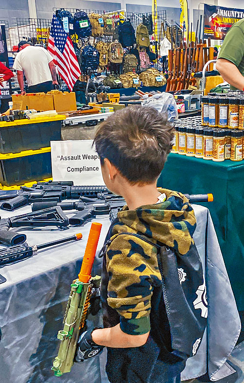 男童在槍展持AR-15玩具槍，觀看攤位展示的真槍。