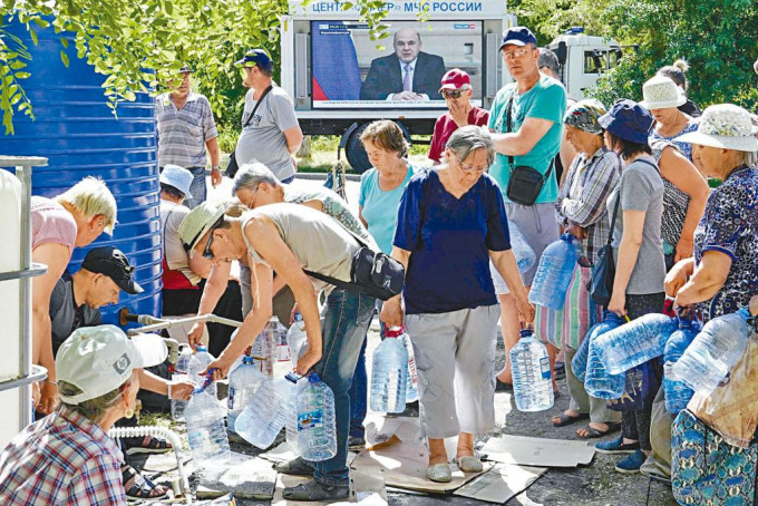 在烏克蘭東南部港市馬里烏波爾，大批民眾日前在街上輪候食水。背後屏幕正在播放俄總理米舒斯京的畫面。