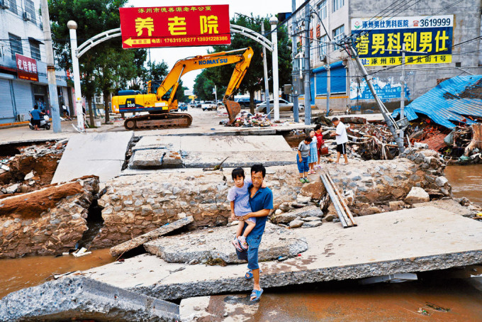 河北涿州洪水退去，滿目瘡痍。一名居民抱着女兒跨過斷橋。