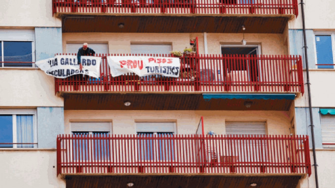 一名男子在公寓外悬挂布条，写着「不要再有观光公寓」。（路透社）