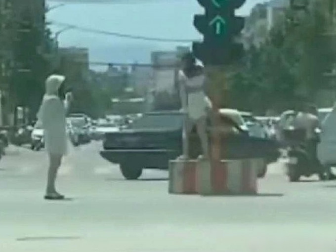 河南一名女子在路口一座红绿灯底座上跳舞，另一名在旁边负责拍片。　影片截图