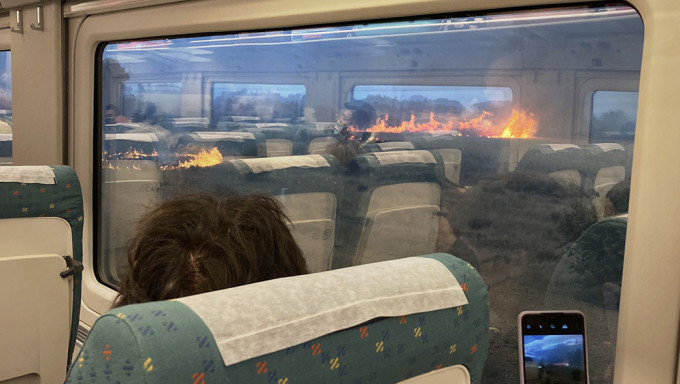 乘客在停滞的列车窗外两侧看着火焰冲天的山火感到不知所措。网图