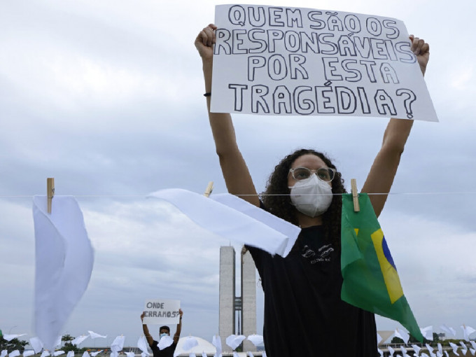 巴西逾60万人感染新冠肺炎后死亡，有民众举牌抗议：「谁为惨剧负责？」 （美联社）