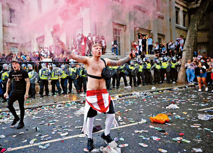 在伦敦特拉法加广场，一名英格兰球迷周日在警察防綫前挥动烟雾弹。　