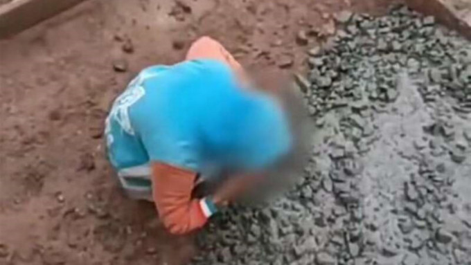 男孩在雨天蹲在地上撿拾混凝土放進嘴裡。