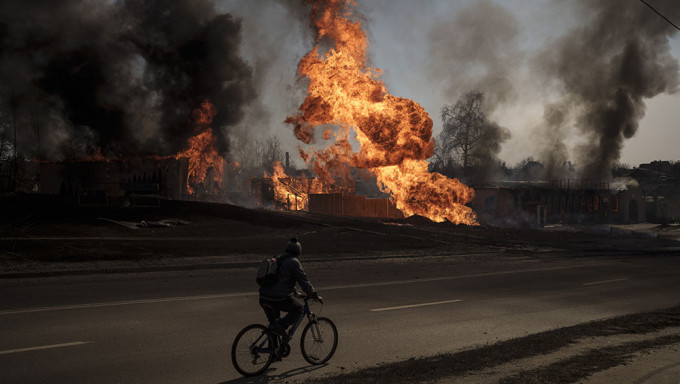 俄军在哈尔科夫发动袭击后，一名男子骑著自行车经过火焰和浓烟。AP