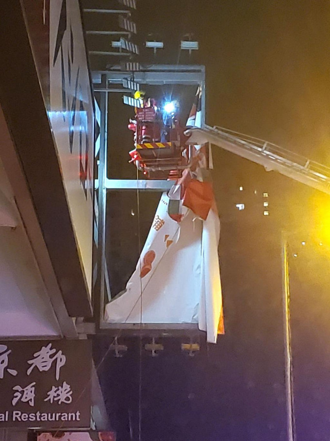 一幅招牌帆布摇摇欲堕，消防架起升降台将其移除。蔡楚辉摄