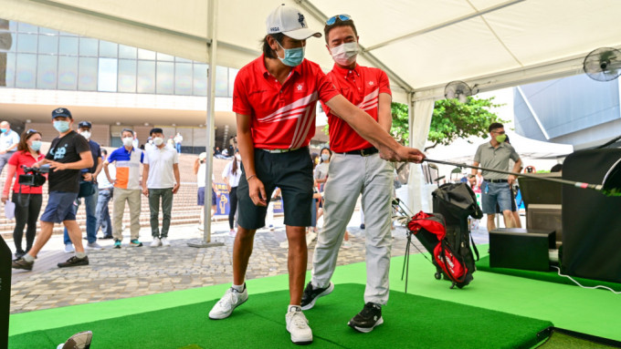   香港高尔夫球代表队成员邓子轩(左)指导下，油尖旺民政事务专员余健强体验电子高尔夫球的乐趣。 公关图片