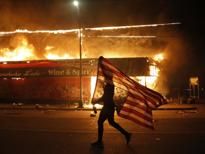 男子举起倒转了的美国国旗在火光中独自向前走。AP