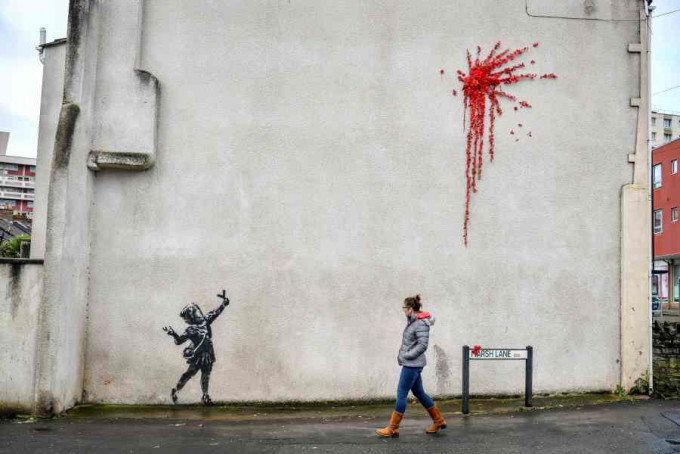 班克西新作小女孩手持弹弓射出一簇红花烟花,遭人涂鸦破坏。AP