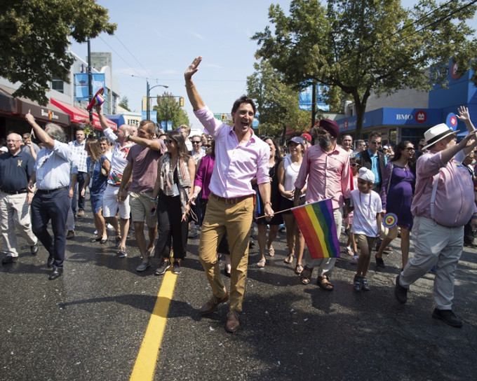 杜魯多手持彩虹旗，與其他參加者在街上並肩而行。AP