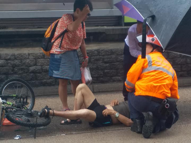 单车男受伤倒地，不少途人走上前为受伤男子撑伞挡雨。  香港突发事故报料区FB/网民Alex Wong‎图