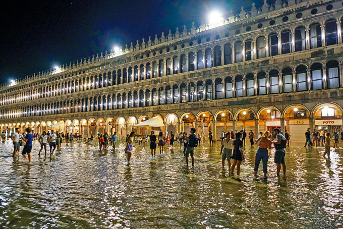 意大利水都威尼斯連日降雨，周日遊人在聖馬可廣場上涉水而行。