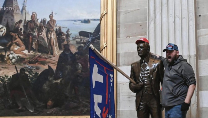暴徒在國會大樓內其中一幅壁畫前拍照留念，畫中顯示，美國立國是靠侵佔印第安人土地。