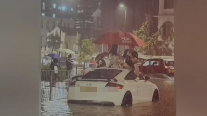洪水围困下不少汽车抛锚， 一对男女爬上车顶撑伞对坐避险， 有网民形容为雨中的浪漫。网片截图