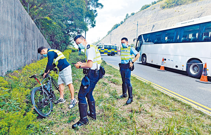 ■警方檢視死者所騎的單車，旁為肇事旅遊巴。