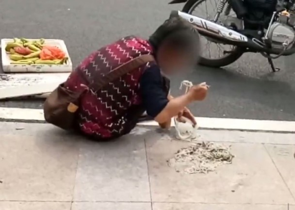 老婦用湯匙吃掉地上的麵條。 網上圖片