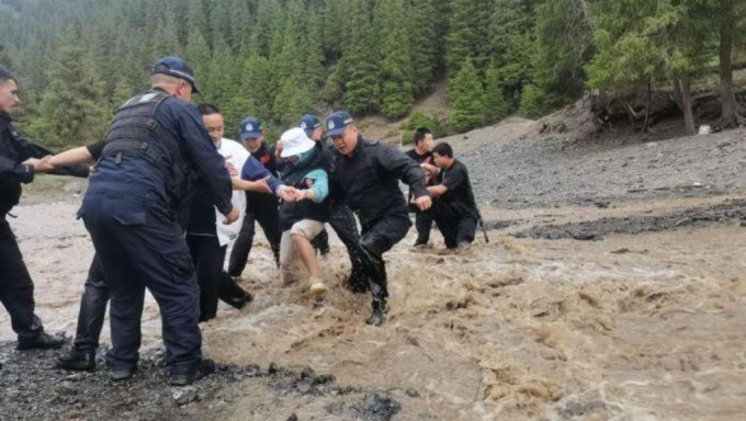 民警以手拖手方式帶領被困遊客跨越水流到安全地點。中新社