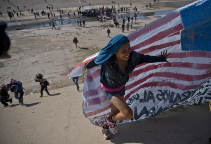 難民手持自行繪製的洪都拉斯和美國國旗，高叫「我們不是罪犯！我們是國際工人！」的口號。(網圖)