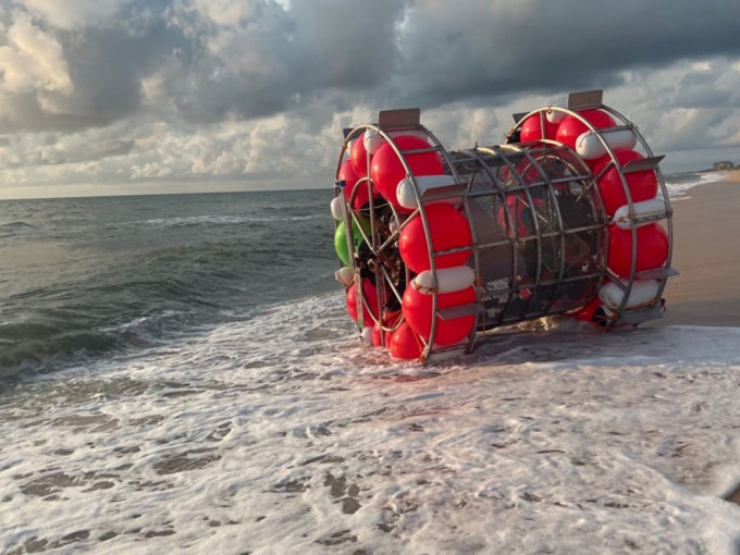 探險家巴盧奇圖以浮桶裝置海上步行到紐約，但設備故障被沖上海灘擱淺。網圖