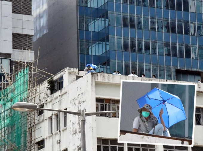 男子持伞危站大厦天台。